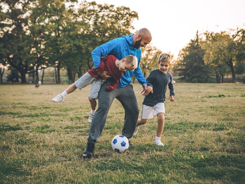 Dad playing soccer with sons in a field.