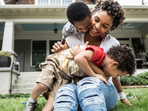 Parent in front of their house, playing with their children on the front lawn.